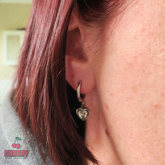 Heart-shaped earring worn by a person with cherry brand logo.